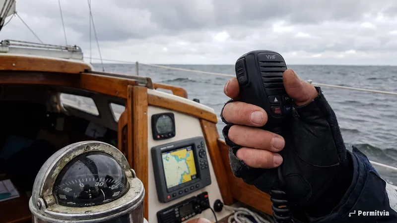 Hand mit UKW-Funkhörer am Steuerstand einer kleinen Segelyacht, Kompass und Kartenplotter, graue Ostsee
